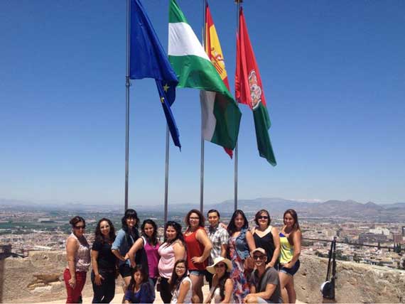 Group of students in front of four flags with a view of a city in the background